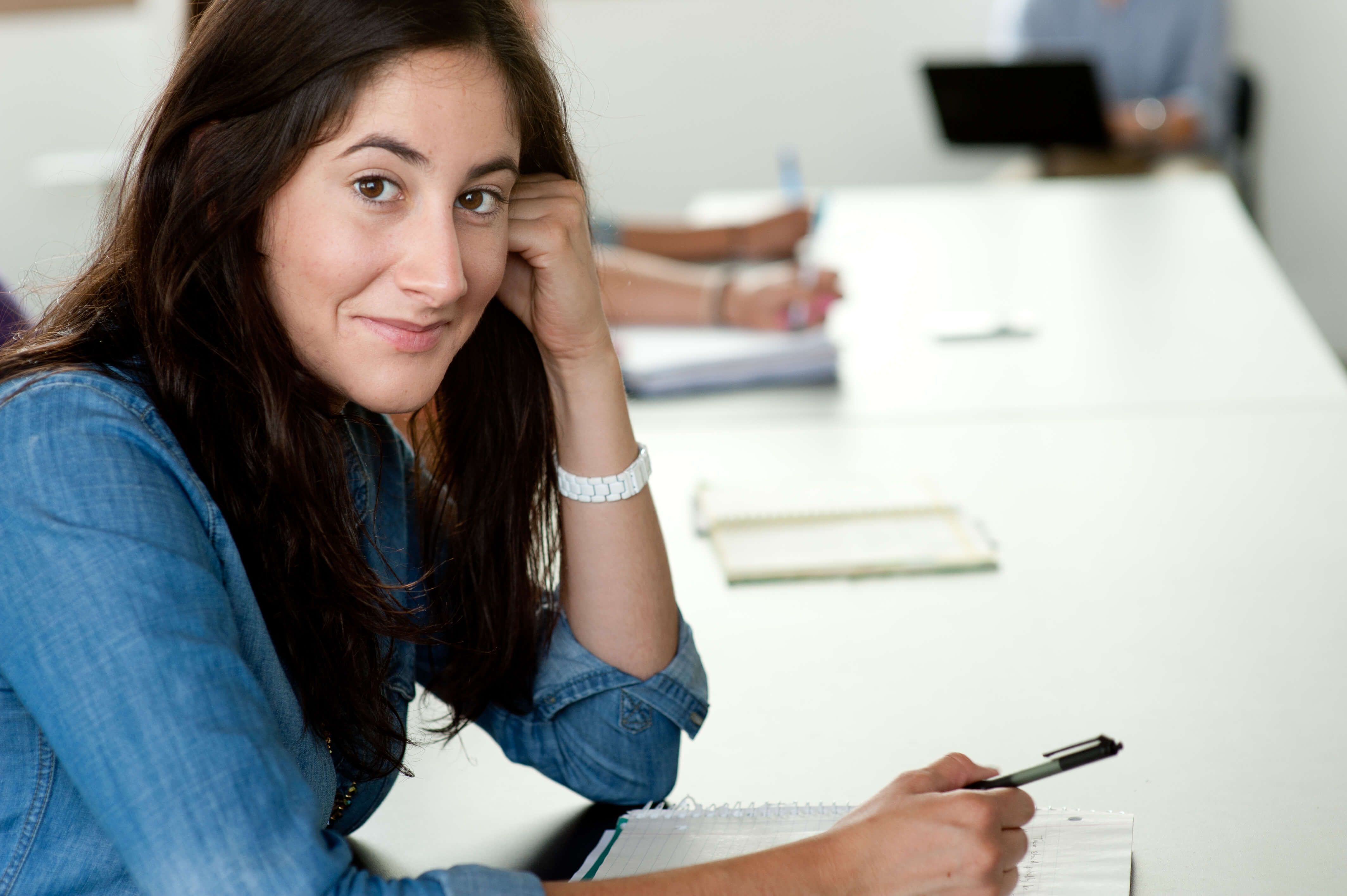 close-up photo of woman with long dark hair sitting at classroom table smiling
