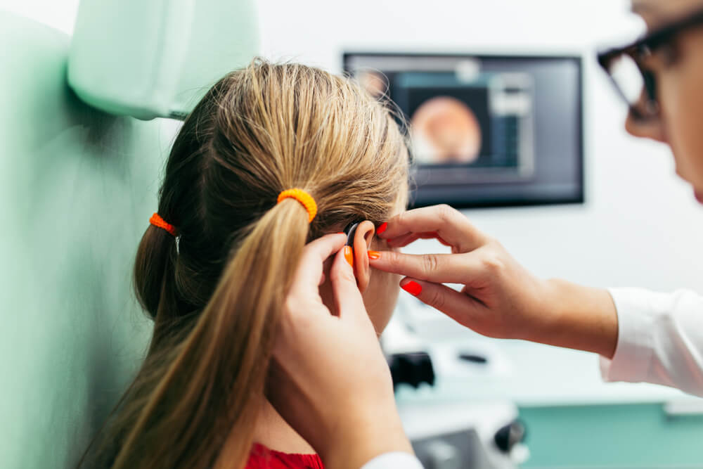 Photograph of an audiologist placing a hearing aid in a young girl's ear.