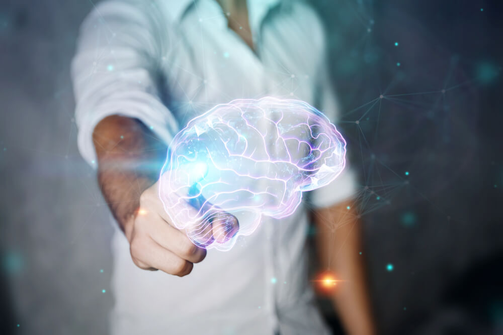 man in white shirt reaches forward to touch hologram of a human brain