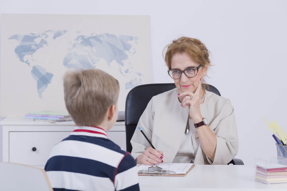 Photograph of an adult woman interviewing a young boy in a classroom or office.