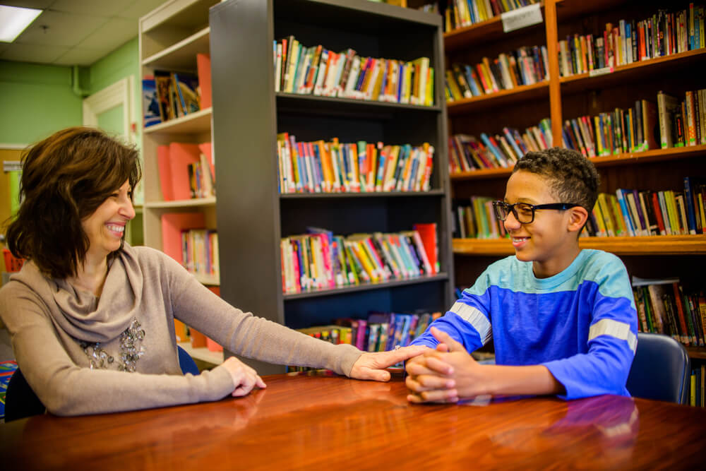 Photograph of a teacher sitting and talking to a little boy in the school library.